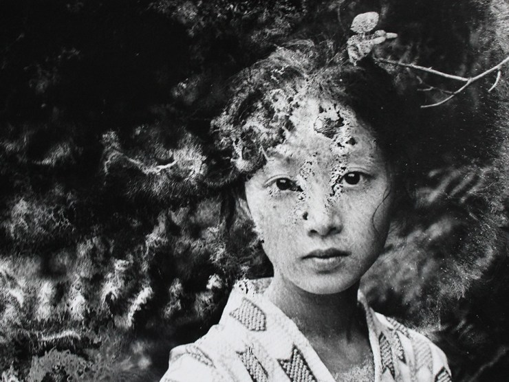 A woman stares at the camera while wearing Japanese dress in this black and white chemically-altered photograph.