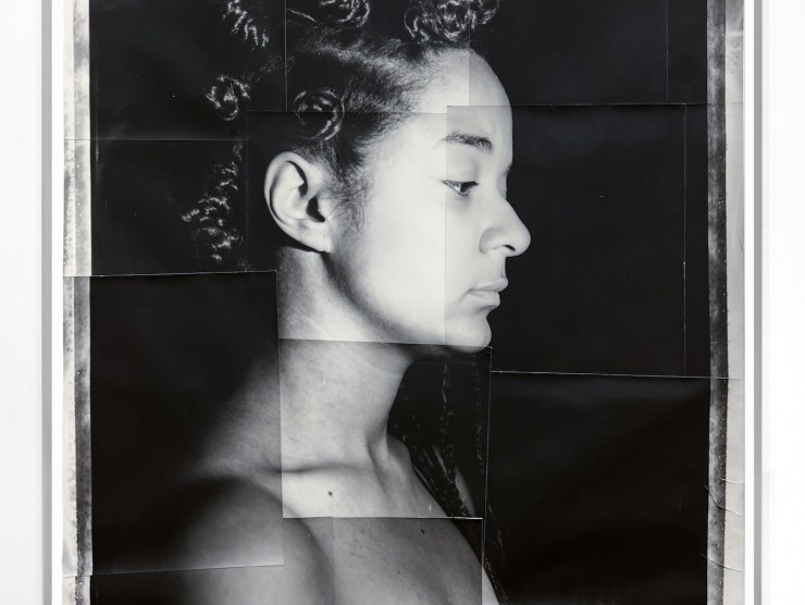A young Black woman with her hair tied up in neat knots is photographed in black and white while she looks away from the camera.