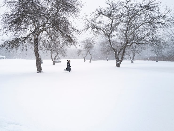 A figure in black runs through a snowy scene among trees