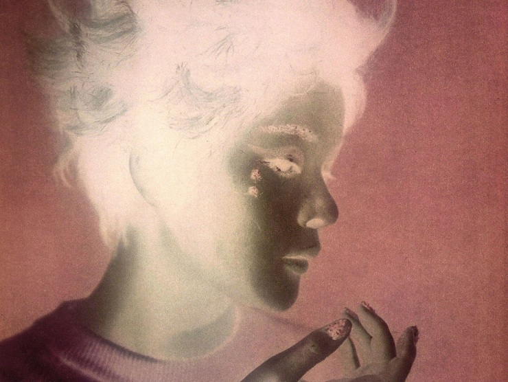 A color image in reversal shows a woman in profile with her hair raising up vertically and her hand poetically held near her face.