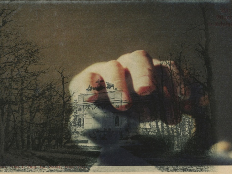 A double exposure where a hand hovers over the image of a building which is surrounded by trees