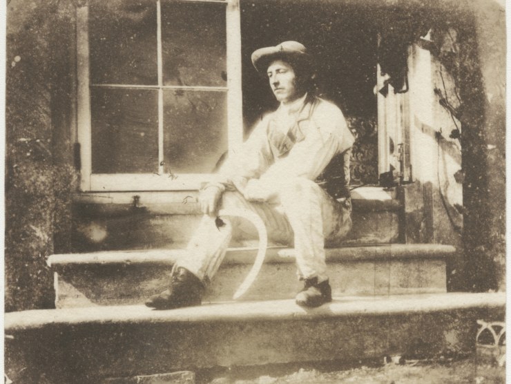 A man sits on steps outside a building in an old-looking sepia photograph