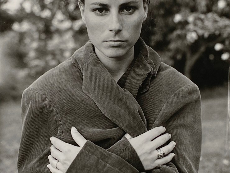 A woman gazes at the camera with a serious expression, while wearing an oversized coat in this black and white photo.