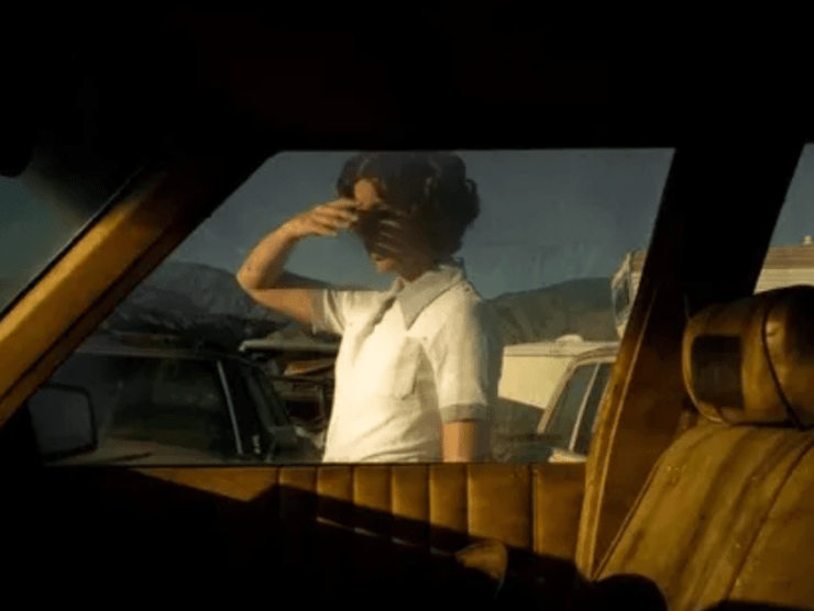 A woman shields her eyes from the sun as she is photographed in color through a car window