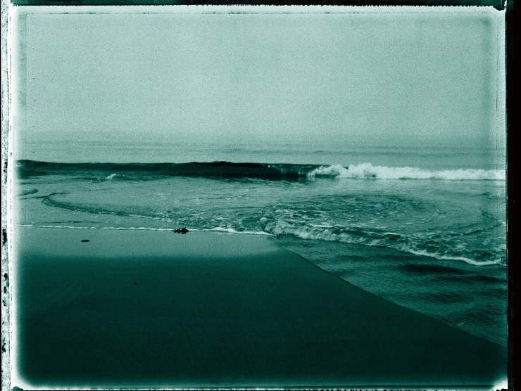 A beach wave is shown rolling in in this cyan-tinted monochromatic photograph.