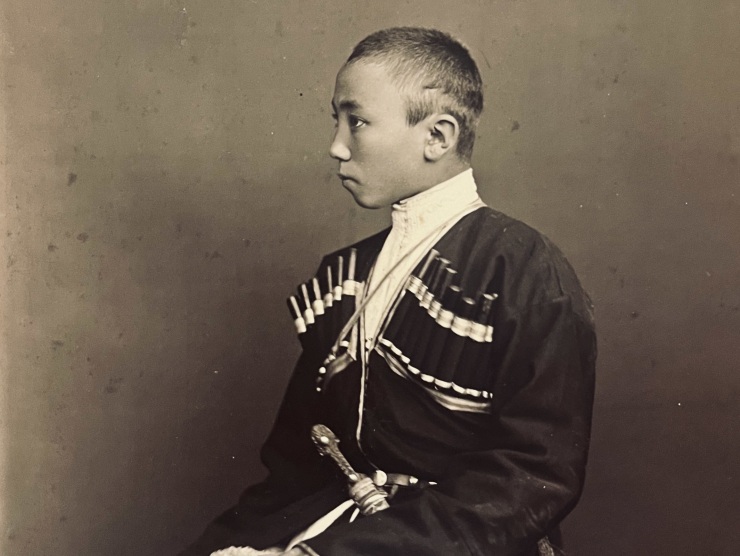 A young man in military dress sits in profile as his portrait is taken in this sepia-toned vintage photograph