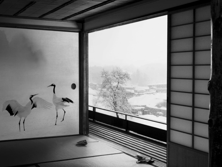 A black and white interior image shows a shimmering painting of cranes and a window with a snow scene outside.