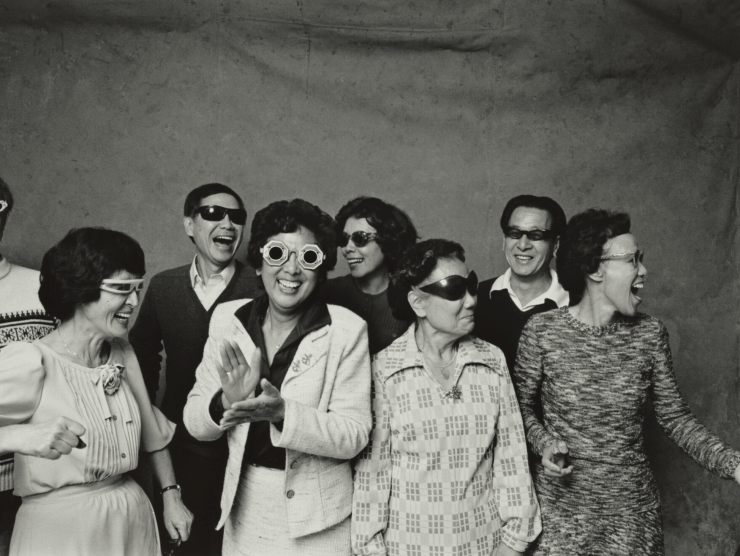 A group of people laugh while wearing different kinds of sunglasses in a black and white photo