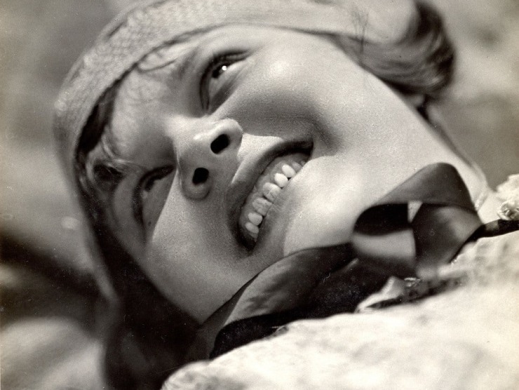 A black and white portrait of a smiling woman's face from below