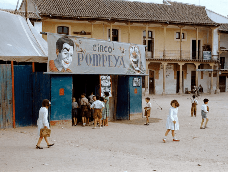 Children walk about on a dusty small town road in front of the circus entrance