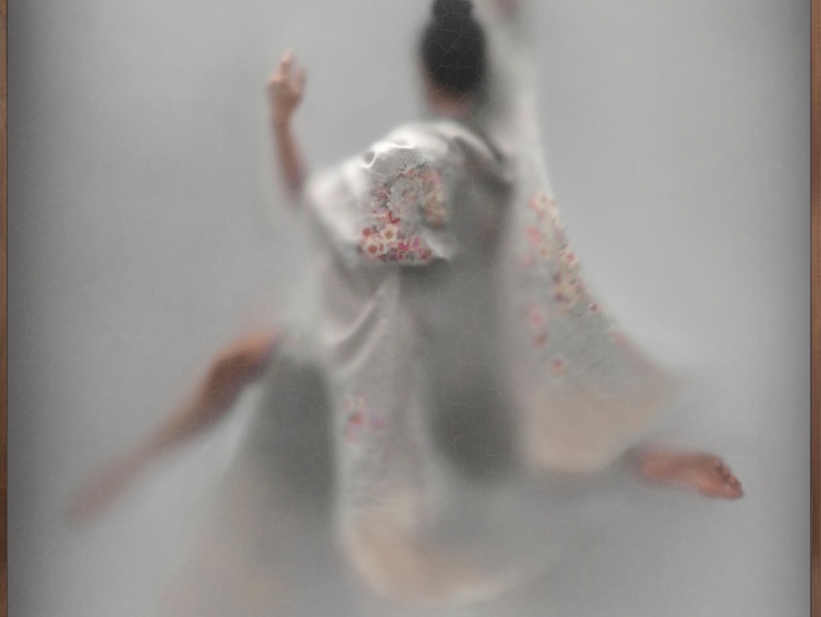A blurry figure wearing a grey satin robe with pink flowers on it dances and is photographed from behind