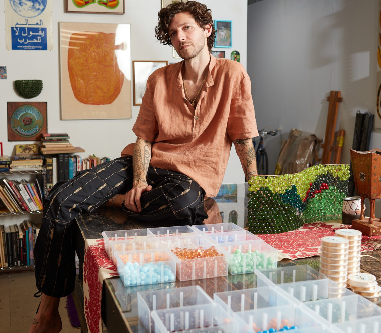 Jordan Nassar sits on a table next to a beaded work
