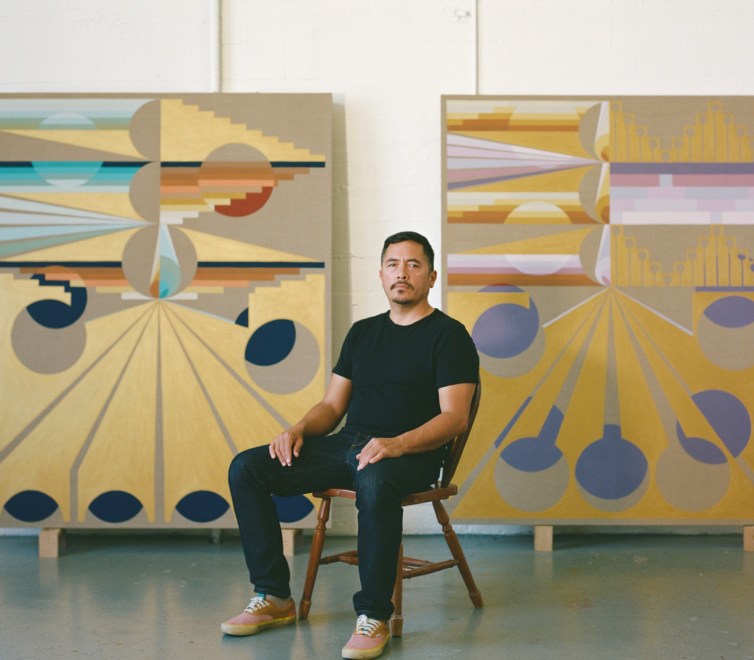 Eamon Ore Giron sitting in front of two of his artworks 