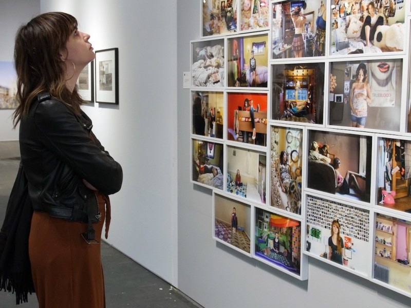 A woman stands in front of a wall of framed color photographs.