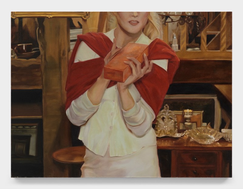 Oil painting on canvas by Shannon Cartier Lucy titled "Woman with Brick," 2022. A woman in a white shirt and skirt whose shoulders are draped with a red sweater holds a brick in front of her chest. The image is closely cropped so that only the bottom half of her face is visible.
