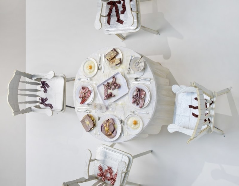 A sculpture by Samara Golden of a breakfast table and chairs mounted to a wall.