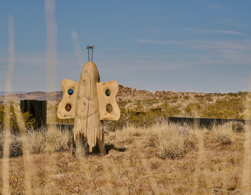 A large wooden sculpture by Dan John Anderson installed in a desert field.