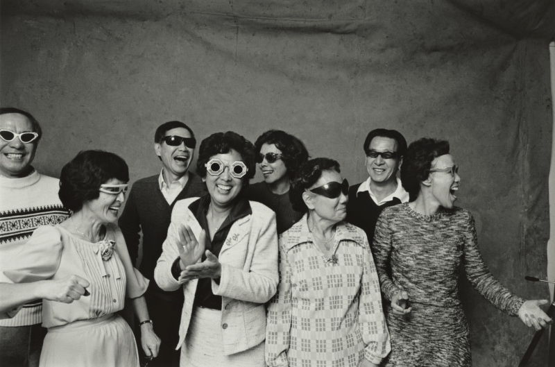 A group of people laugh while wearing different kinds of sunglasses in a black and white photo