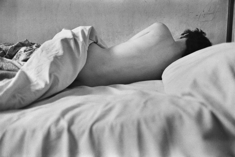 A naked woman is photographed from behind, exposing her back, as she sleeps