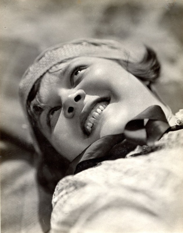 A black and white portrait of a smiling woman's face from below