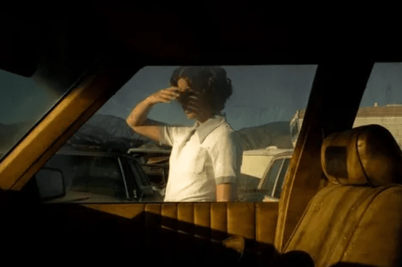 A woman shields her eyes from the sun as she is photographed in color through a car window