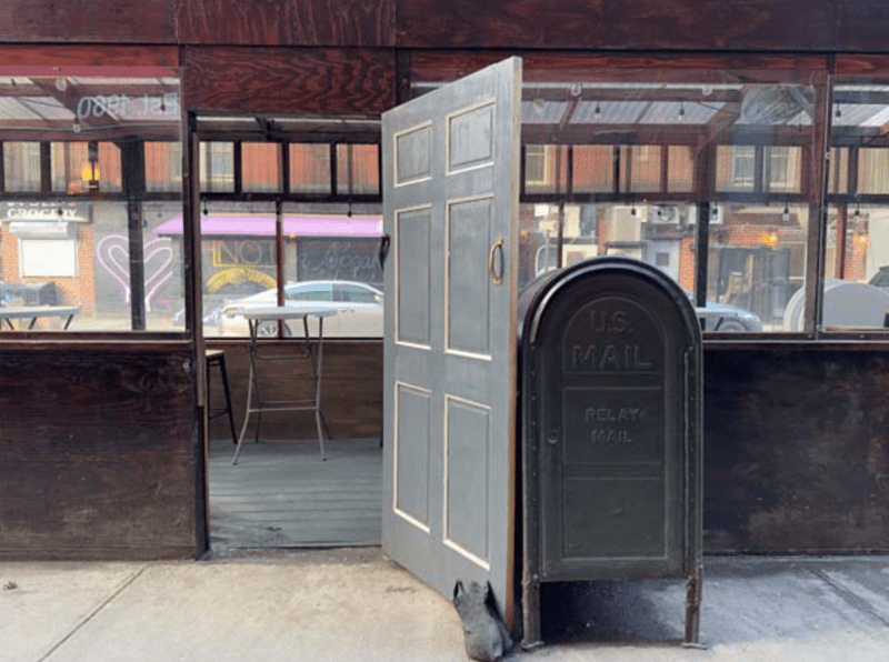 A street-side shed is photographed with the door propped open