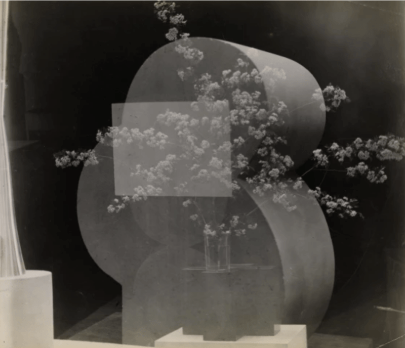 Three negatives are combined to create a superimposition where a vase with many flowers is shown under a rectangle and an abstract sculpture, all in black and white