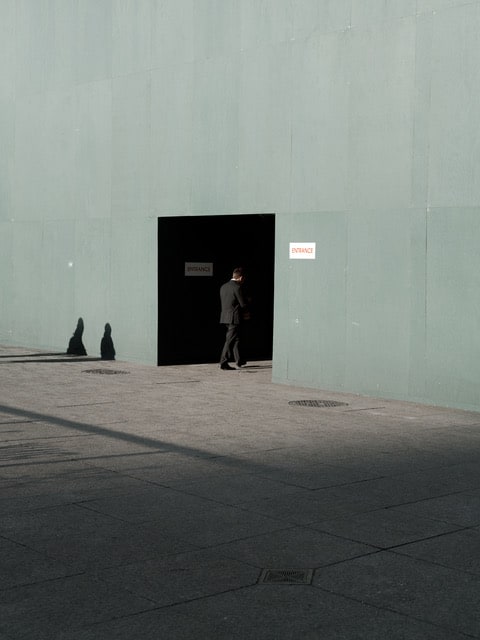 A man enters a darkened doorway at the light hits the green building he is entering.
