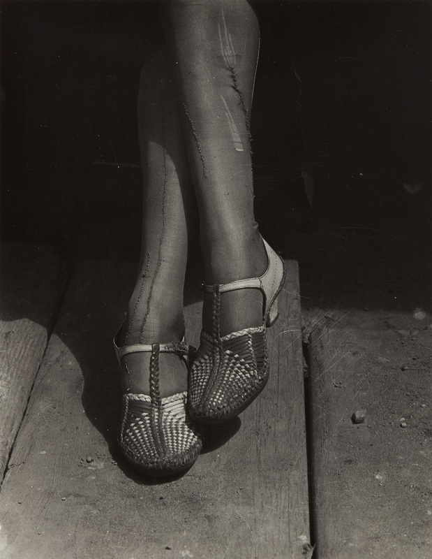 Black and white photograph of women's legs crossed and the woven detail of her shoes.