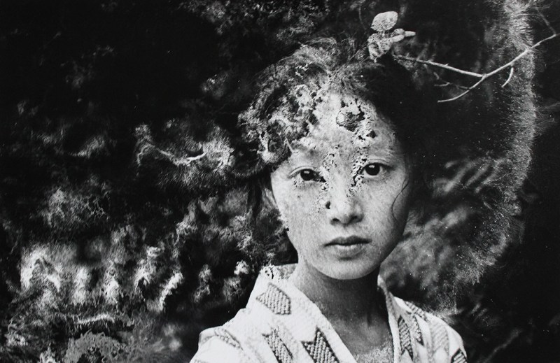 A woman stares at the camera while wearing Japanese dress in this black and white chemically-altered photograph.