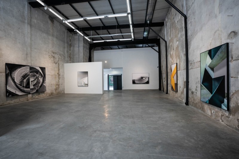 The concrete and cavernous interior of Ungallery is shown in this color photograph, with large artworks on the gallery walls.