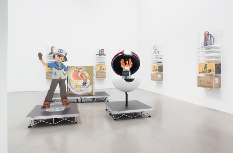 Installation of Blockchain future states at Petzel Gallery in 2016, featuring several dream boxes hanging on the walls and a large cut out of Ash from Pokemon on a pedestal with an open pokeball next to him.