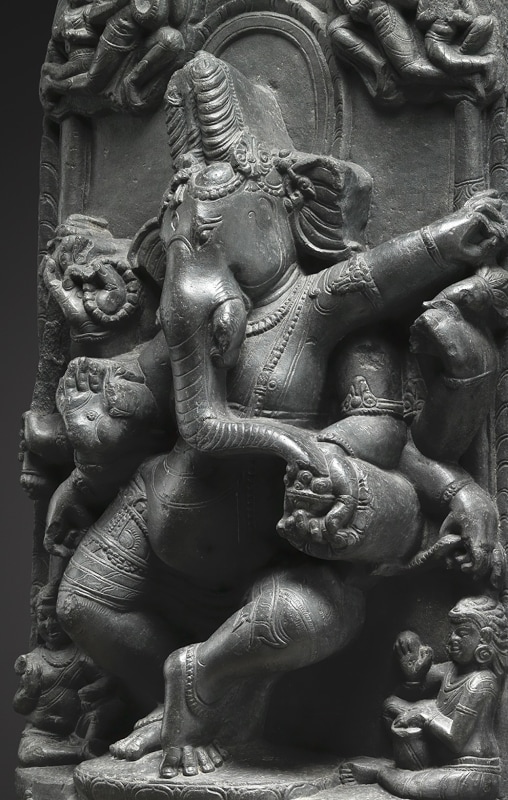 Watched by two cloud-borne celestial garland bearers, eight-armed elephant-headed Ganesha dances in a lively attitude on a lotus flanked by his recumbent rat vehicle and a kneeling donor figure.