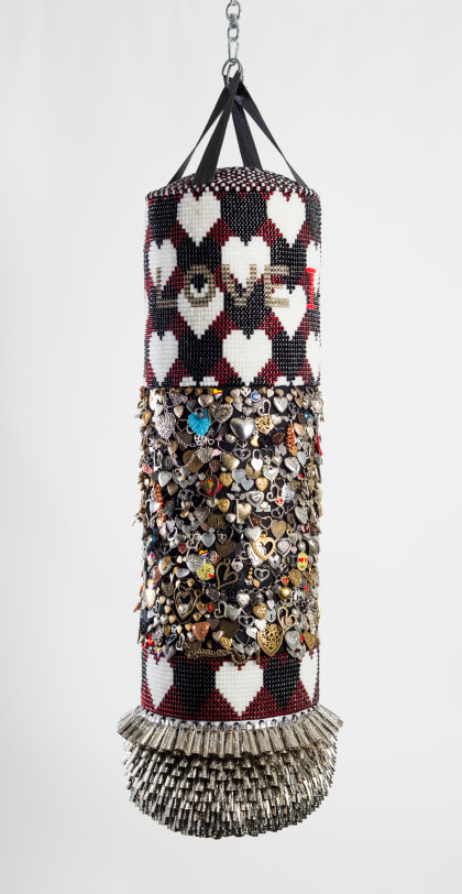 Jeffrey Gibson LOVE IS THE DRUG, 2017 Repurposed vinyl punching bag, glass beads, found and collected mixed metal charms, cotton, artificial sinew, tin jingles, acrylic felt 55 x 13 in (139.7 x 33.0 cm)