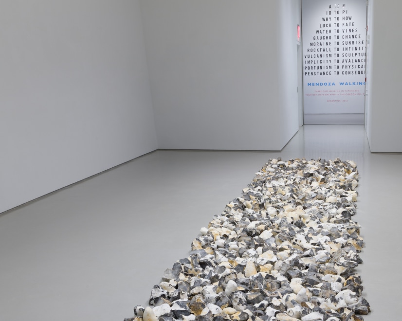 rectangular floor sculpture made up of pieces of flint rock with a vinyl wall text artwork in the background 