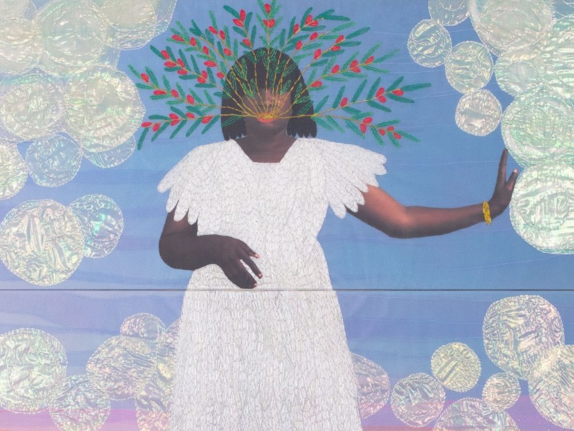 A black woman wearing a white dress has embroidered branches emerging from her mouth. One hand is bent at her wait and the other is reaching out. The background is blue and pink and has embroidered pearl white circles. 