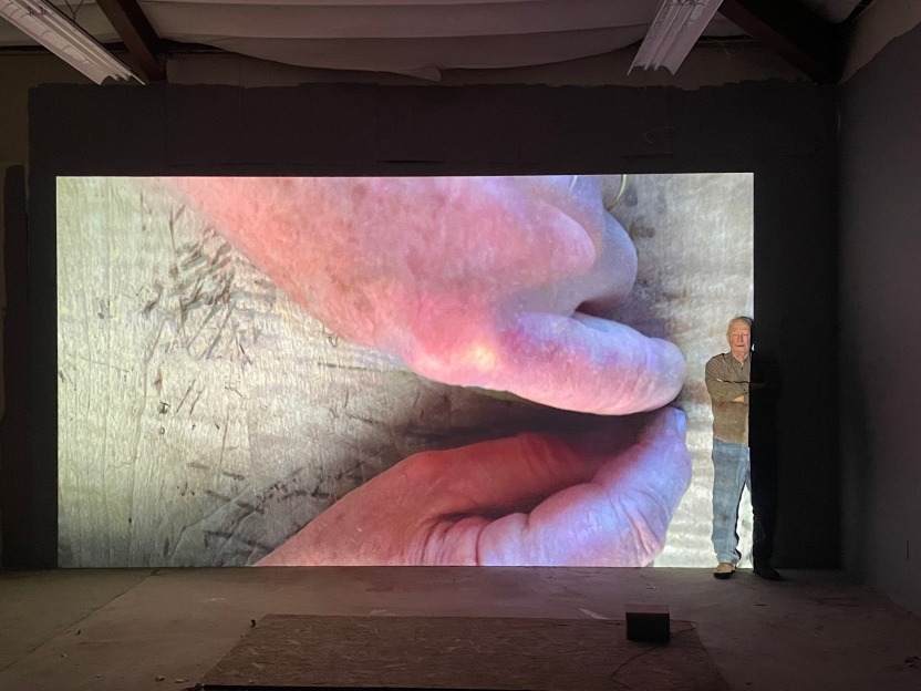 Bruce Nauman stands in front of a projection from his new video work "His Mark"