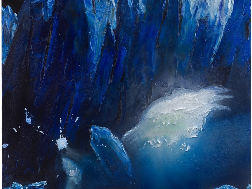 Craggy glaciers of varying blue hues tower over a man in a canoe as he paddles away from a piece of falling ice