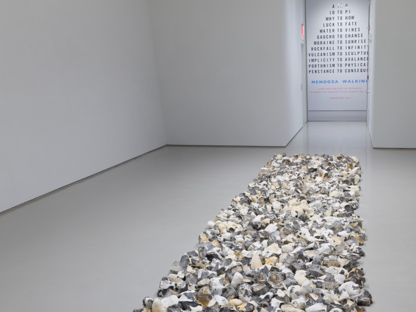 rectangular floor sculpture made up of pieces of flint rock with a vinyl wall text artwork in the background 