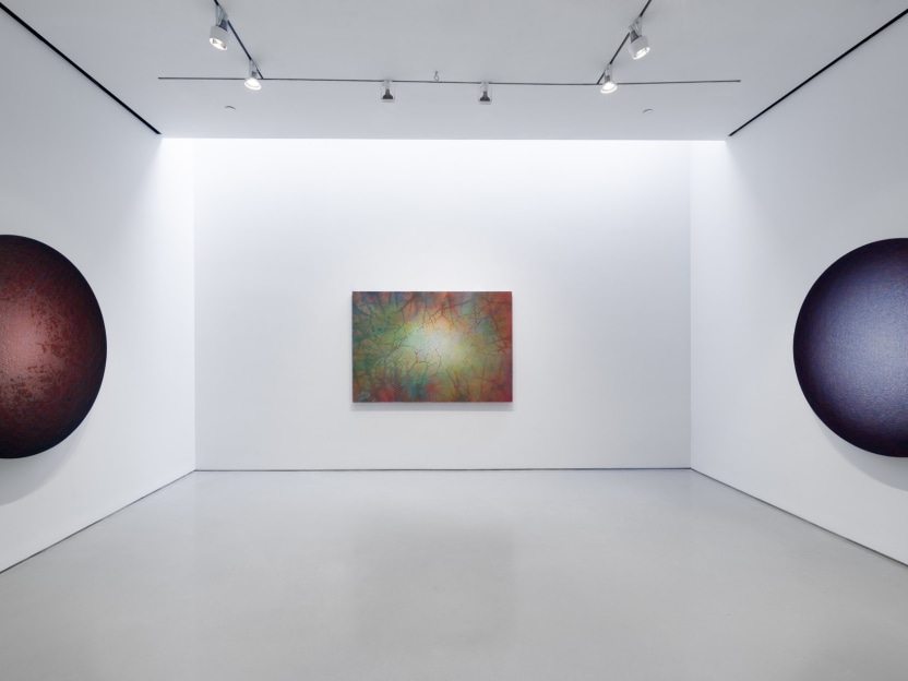 art gallery with one work on each wall, on the left a red tondo painting, in the center an abstract square painting, and on the right a blue tondo painting