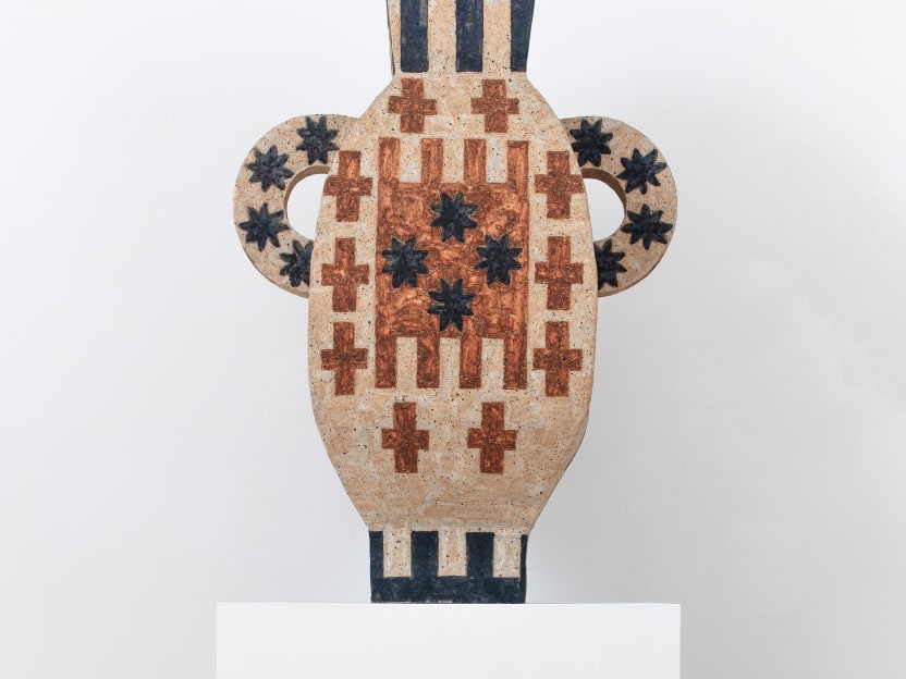 ceramic sculpture in tones of sand, orange, and black with geometric pattern on a white pedestal 