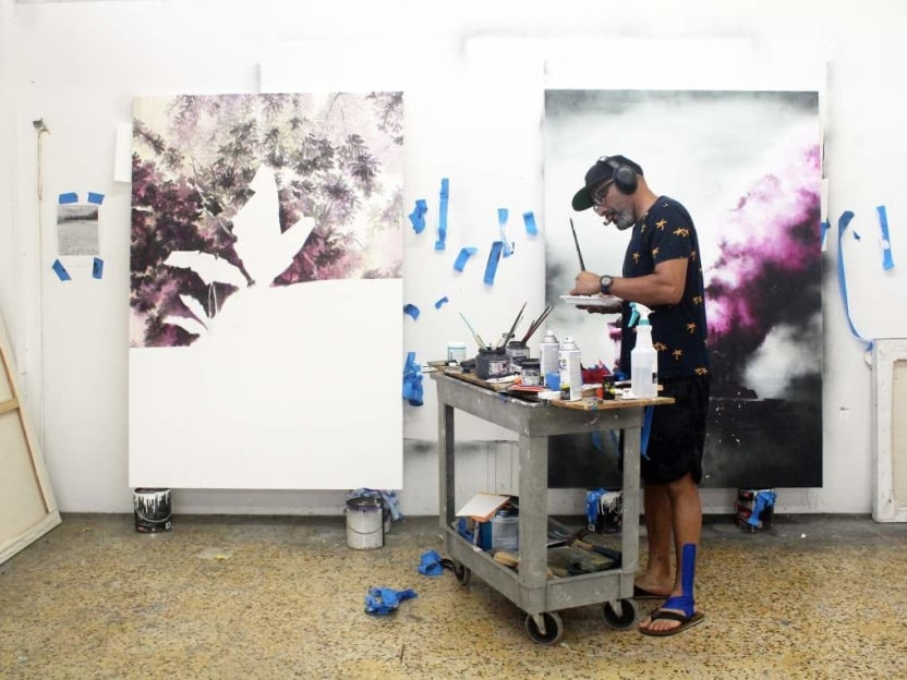 an artist mixes paints on a pallet in his studio with two canvases in progress on the wall