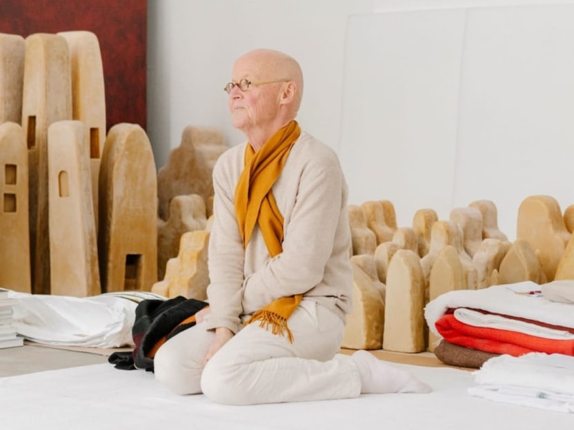 Wolfgang Laib sits on the floor, surrounded by small wax sculptures. 