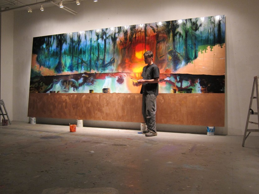Man standing in front of a large half-finished painting in a empty studio