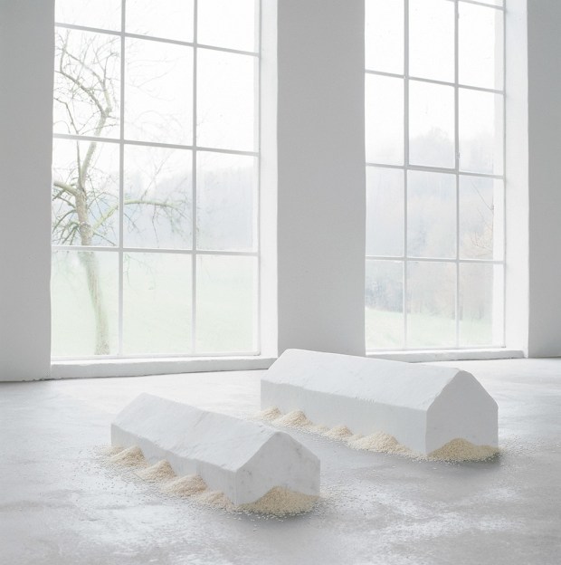 Two miniature white marble houses in an empty white room surrounded by rice