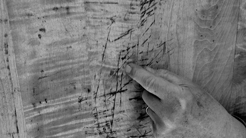 video still showing a close up of a hand with the index finger making an invisible mark on a piece of plywood