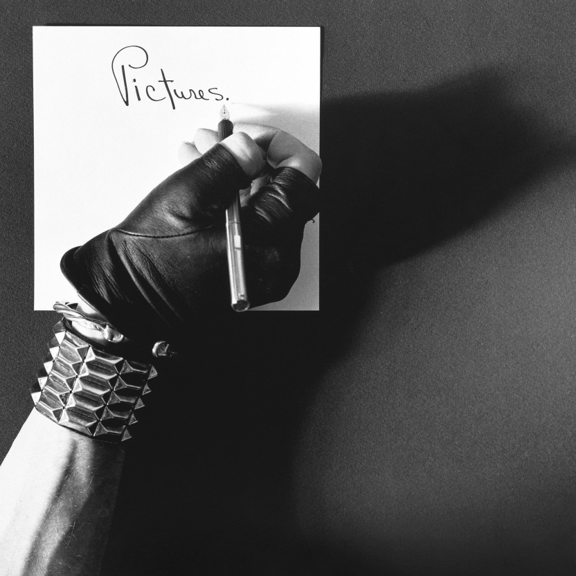 Hand in leather glove and bracelet writing "Pictures."