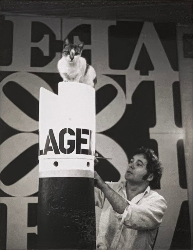 Robert Indiana working on the sculpture Flagellant, with Love Rising in the background. A cat sits atop the sculpture