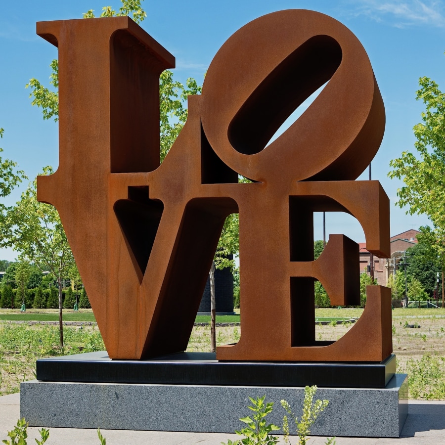 LOVE is a 96 by 96 by 48 inch Cor-Ten steel sculpture. The work consists of the letter "L" and a tilted letter "O" above the letters "V" and "E."