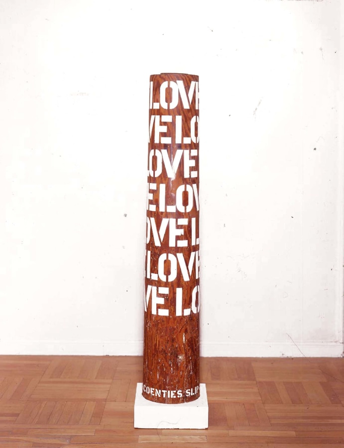 A column with five rows of the word love in gesso stenciled letters wrapping around the upper two thirds of the sculpture. 